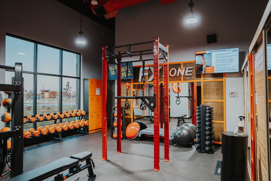 HOTWORX FX Zone — functional training floor with neon orange branding, sauna pods, and red rig